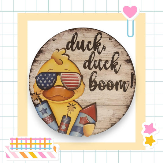 A wooden sign with a duck wearing sunglasses and holding fireworks, accompanied by the text "duck, duck boom!"