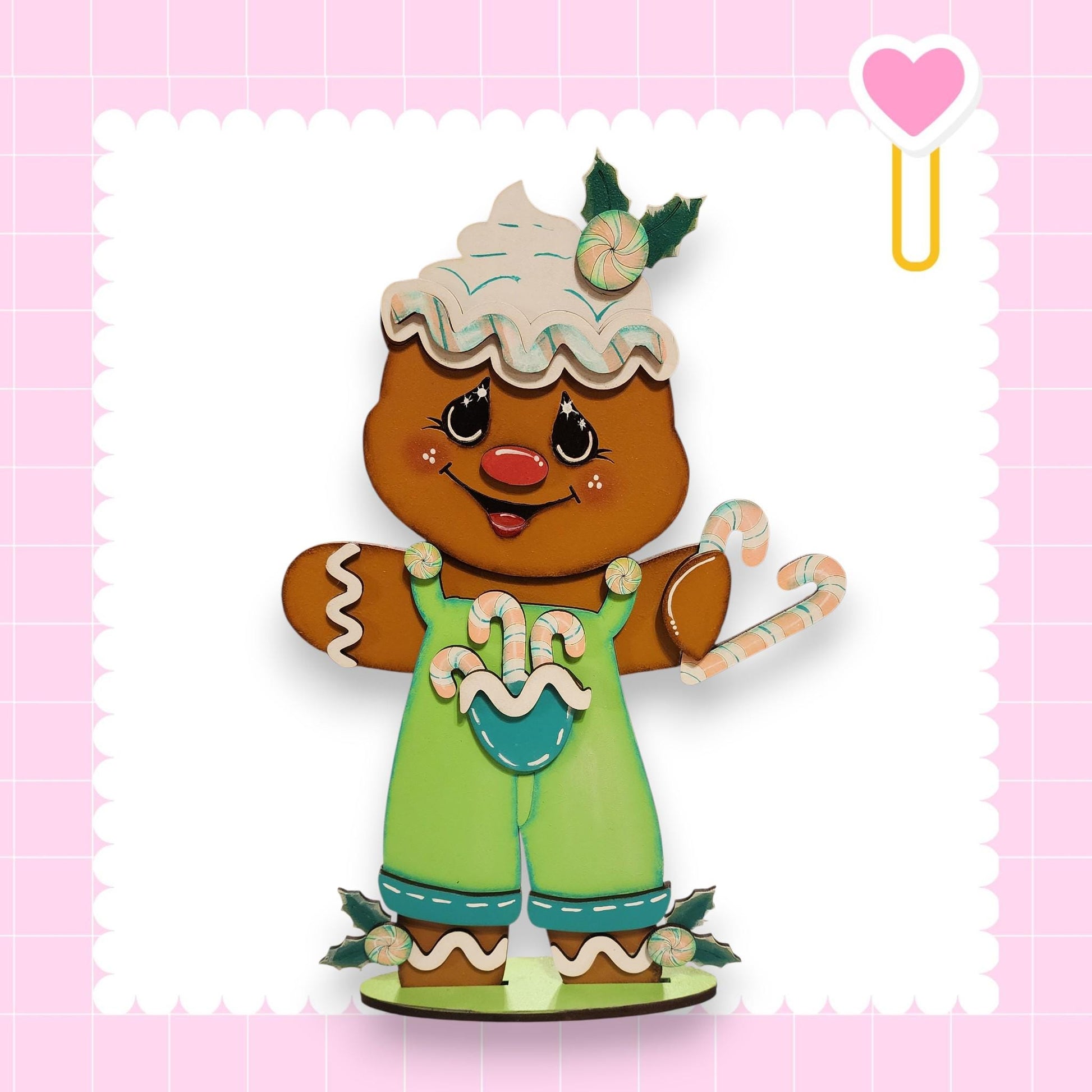 A gingerbread man wearing a green outfit and holding candy cane and a heart-shaped object, set against a pink background with a scalloped edge.