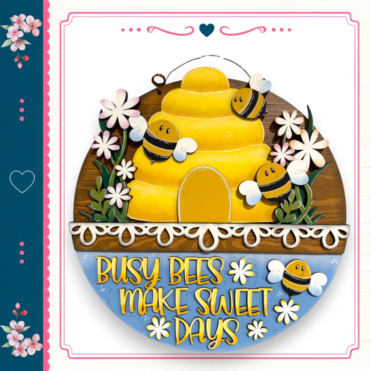 A wooden sign with a bee and flower design, surrounded by the text "Busy bees make sweet days"