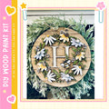 A decorative wreath made of wood and adorned with various flowers and leaves, including a large letter "H" in the center.