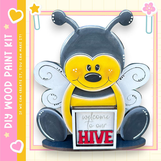 A wooden paint kit depicting a cartoon bee with a sign that says "welcome to our hive".