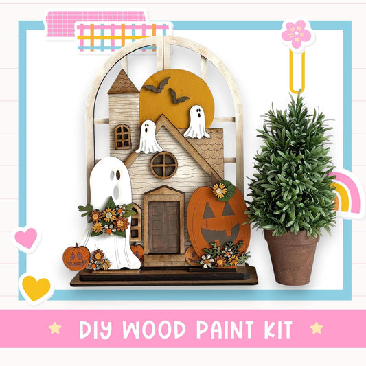 a DIY wood paint kit for creating a Halloween-themed decoration, including a wooden house, ghost decorations, and a potted plant.