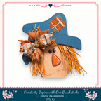 A wooden scarecrow with a blue hat and orange patch, featuring a plaid bow and straw tassels, is displayed against a white background.