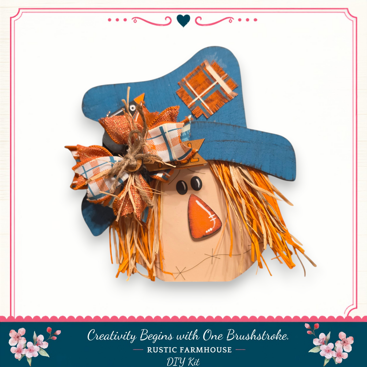 A wooden scarecrow with a blue hat and orange patch, featuring a plaid bow and straw tassels, is displayed against a white background.
