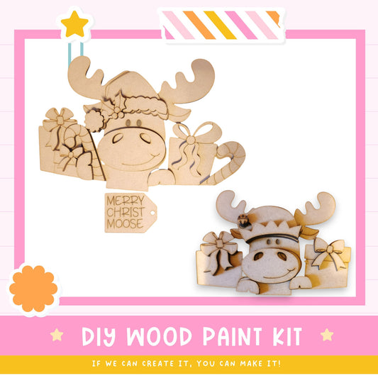 The image is a DIY wood paint kit featuring two wooden moose figures, one larger and one smaller, with bows and presents around them. The kit appears to be designed for creating wooden decorations or toys.