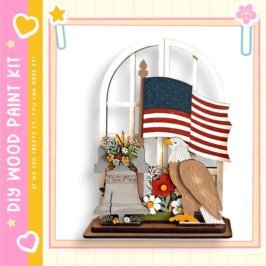 A wooden sculpture depicting a bald eagle, a bell, and an American flag, with flowers and a plaque in the foreground.