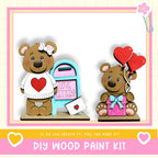 two wooden teddy bears, one standing and one sitting, with heart-shaped balloons attached to them. The teddy bears are positioned next to a mailbox with a "Love Letters" sign. The image also includes text that says "DIY WOOD PAINT KIT" and "If we can create it, you can make it!"