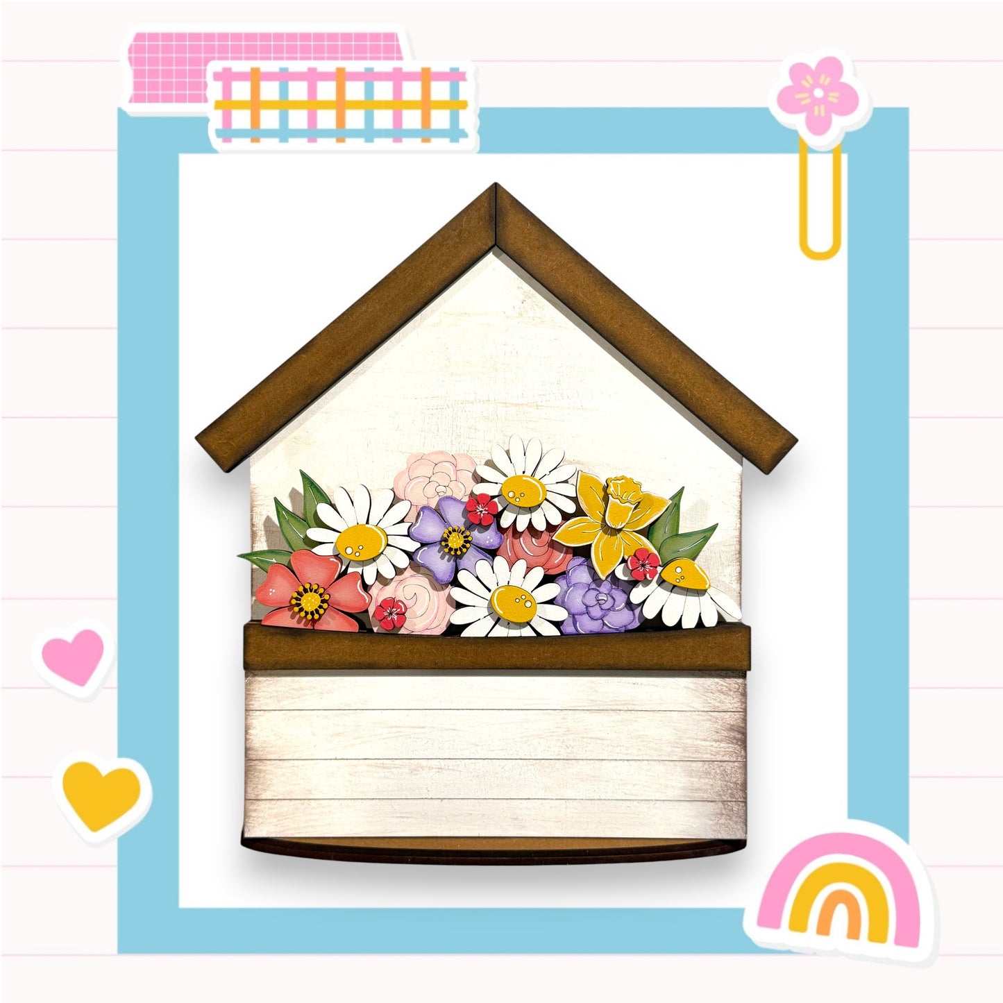 A wooden house-shaped structure with a flower arrangement on top, surrounded by various colorful and whimsical elements such as hearts, a rainbow, and a paper clip.