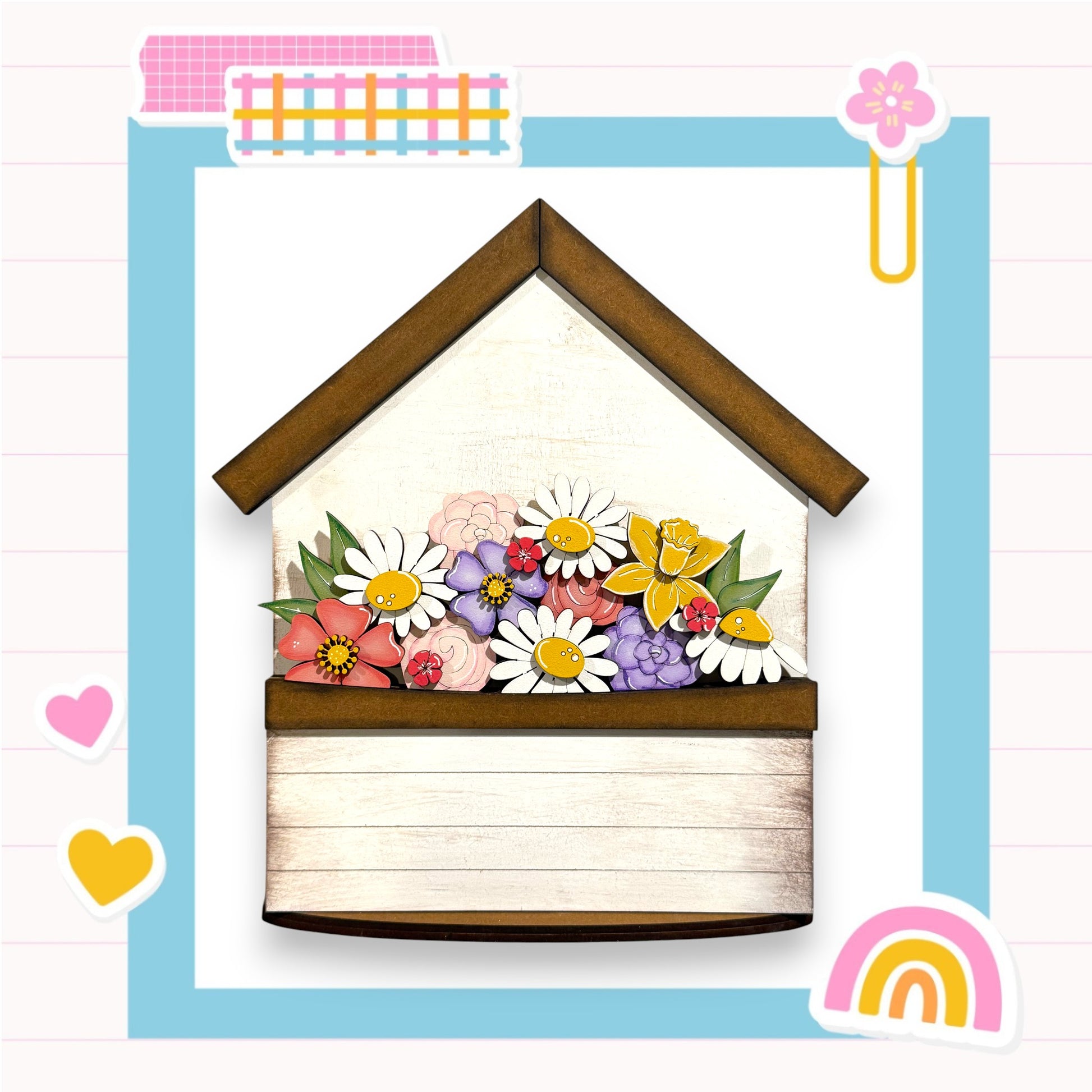 A wooden house-shaped structure with a flower arrangement on top, surrounded by various colorful and whimsical elements such as hearts, a rainbow, and a paper clip.