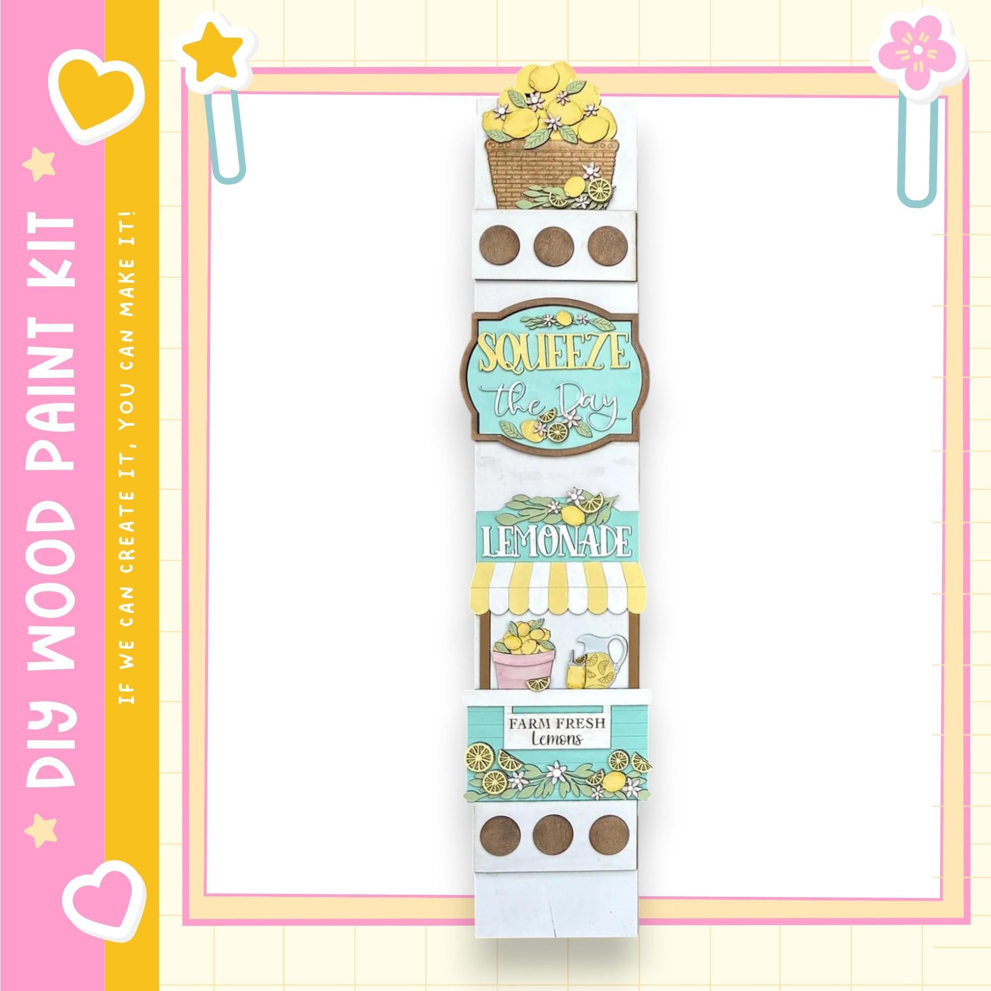 A vertical display featuring a lemonade sign, lemonade glasses, and a basket of lemons, all set against a pink and yellow background.