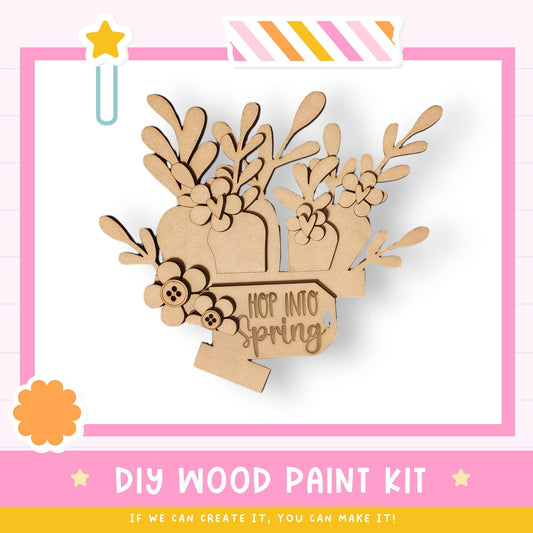 The image is a promotional poster for a DIY wood paint kit, featuring a wooden flower design with the text "HOP INTO SPRING" and a star symbol.