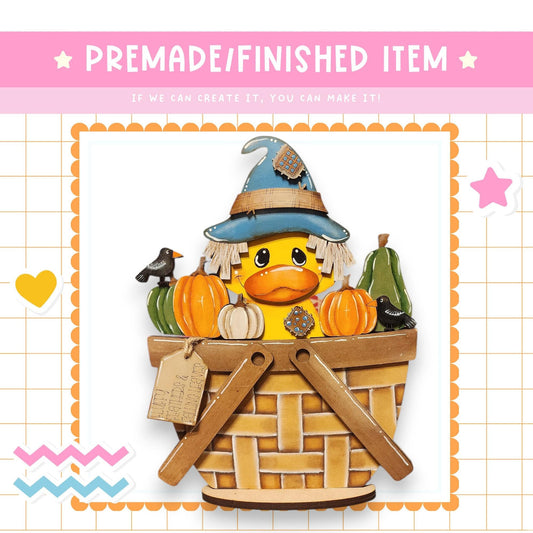 A whimsical illustration of a duck wearing a witch's hat, surrounded by pumpkins and a bird, sitting in a basket.