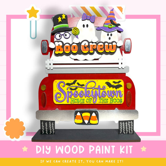 The image is a Halloween-themed DIY wood paint kit featuring a decorated truck with ghostly figures and a sign that says "Spookytown Home of the Boo".