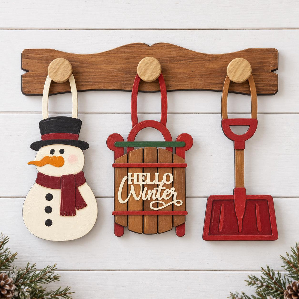 a wooden board with three wooden ornaments hanging on it, including a snowman, a sled, and a shovel.