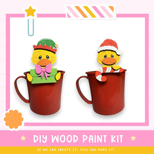 two cute duck figurines, one wearing a green hat and the other wearing a Santa hat, sitting inside red mugs. The image also includes text that says "DIY WOOD PAINT KIT" and "IF WE CAN CREATE IT, YOU CAN MAKE IT!"