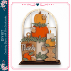 The image is a decorative piece featuring a wooden frame with a window, displaying a collection of autumn-themed items such as pumpkins, leaves, and a candle.