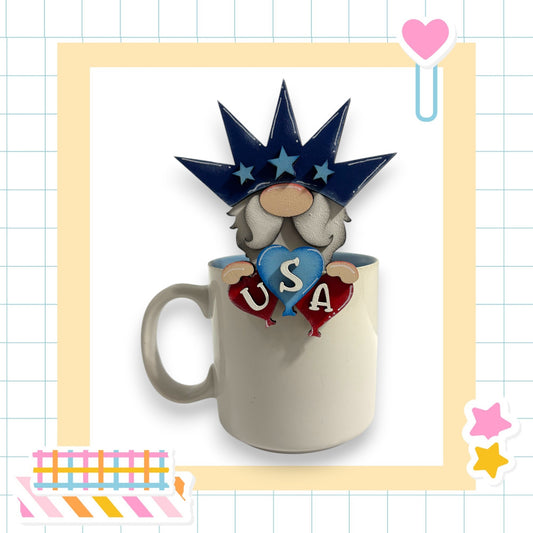 A mug with a figurine of a smiling gnome wearing a crown and holding a heart and balloons, with the word "USA" written on the mug.