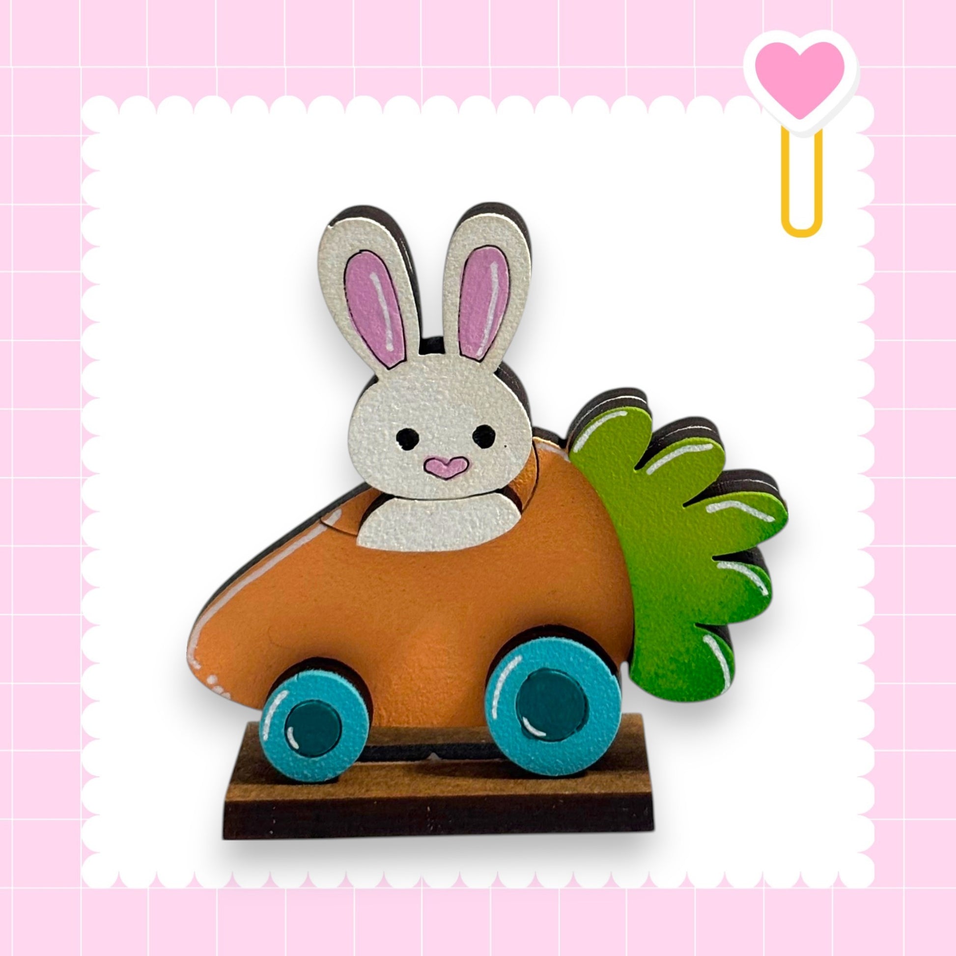 A wooden toy car with a bunny figure on it, set against a pink background with a heart shape.
