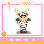 a wooden toy moose with antlers, wrapped in white cloth, and standing on a wooden base. The image is part of a DIY wood paint kit, and it is described as a kit for creating a wooden toy moose.