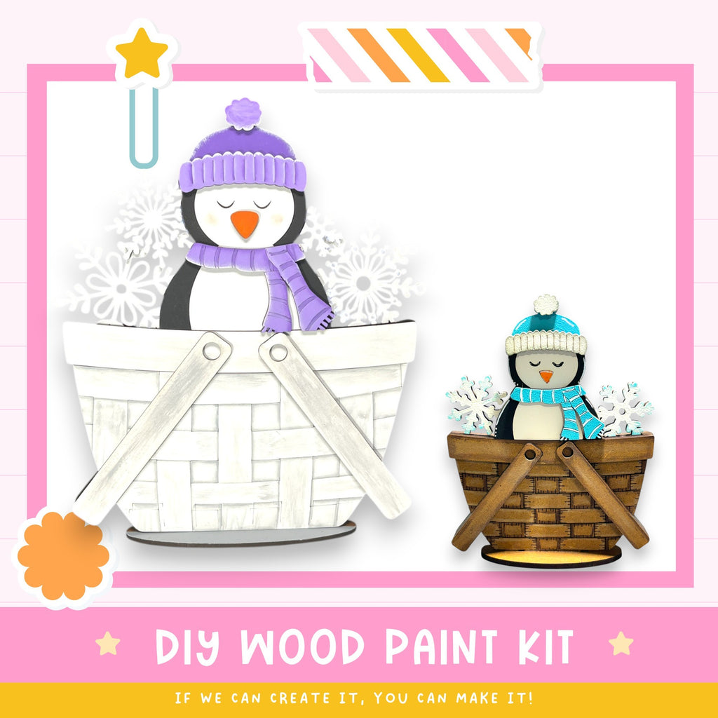 a DIY wood paint kit, with a penguin and a snowman in a basket, along with a pink and white striped border. The kit appears to be made of wood and is designed for creating custom wooden figures.
