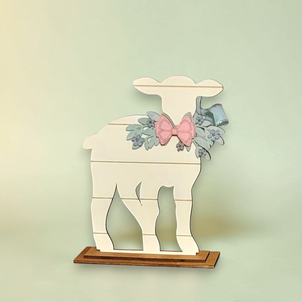 A white wooden lamb figure with a bow and floral decorations is displayed on a wooden base.