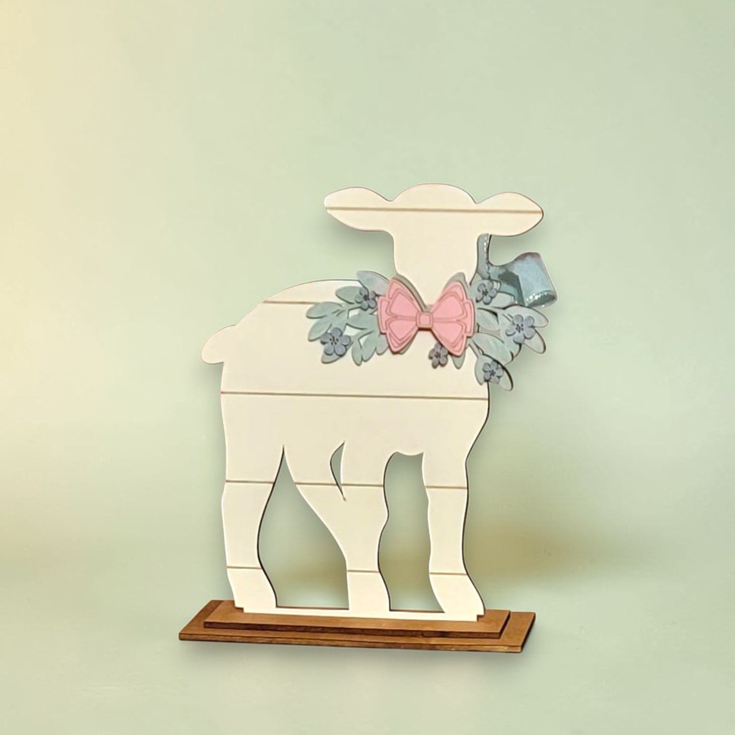 A white wooden lamb figure with a bow and floral decorations is displayed on a wooden base.
