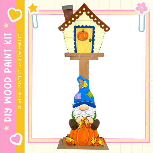 A gnome figurine is sitting on a wooden post, holding a pumpkin and surrounded by autumn leaves.