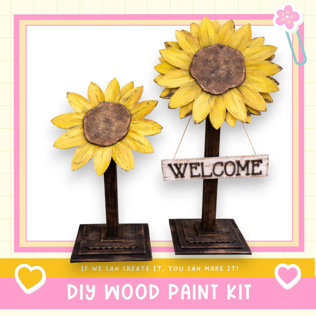 two wooden sunflower sculptures, each with a wooden sign attached to them. The sign reads "WELCOME". The sculptures are placed on a wooden stand, and the background is a pink and white checkered pattern. The image also includes text that says "DIY WOOD PAINT KIT" and "If we can create it, you can make it!"