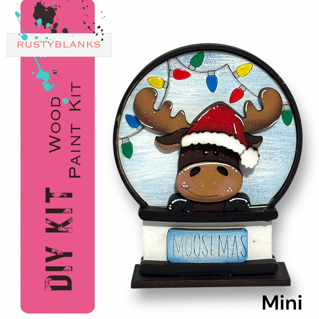 a DIY kit for a Moosemas snow globe, which includes a wooden frame and a moose figurine wearing a Santa hat.
