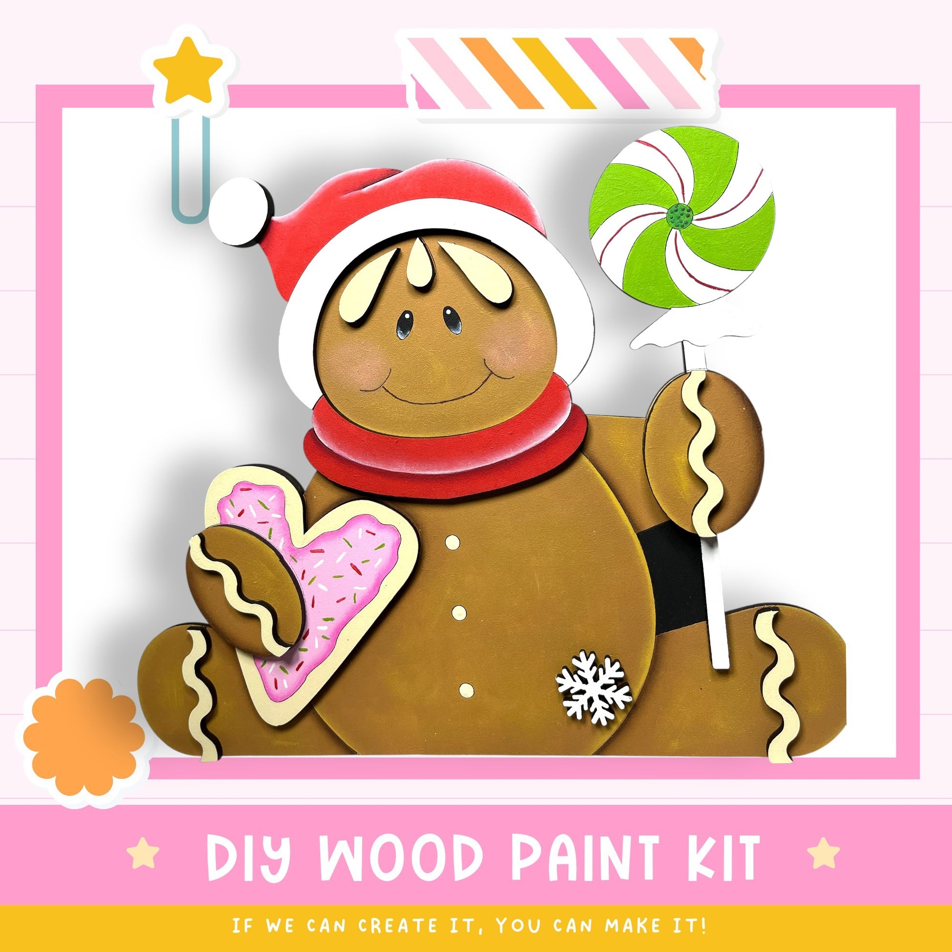 A wooden gingerbread man figure wearing a red hat and holding a heart-shaped doughnut and a candy cane, with a "DIY WOOD PAINT KIT" sign in the background.