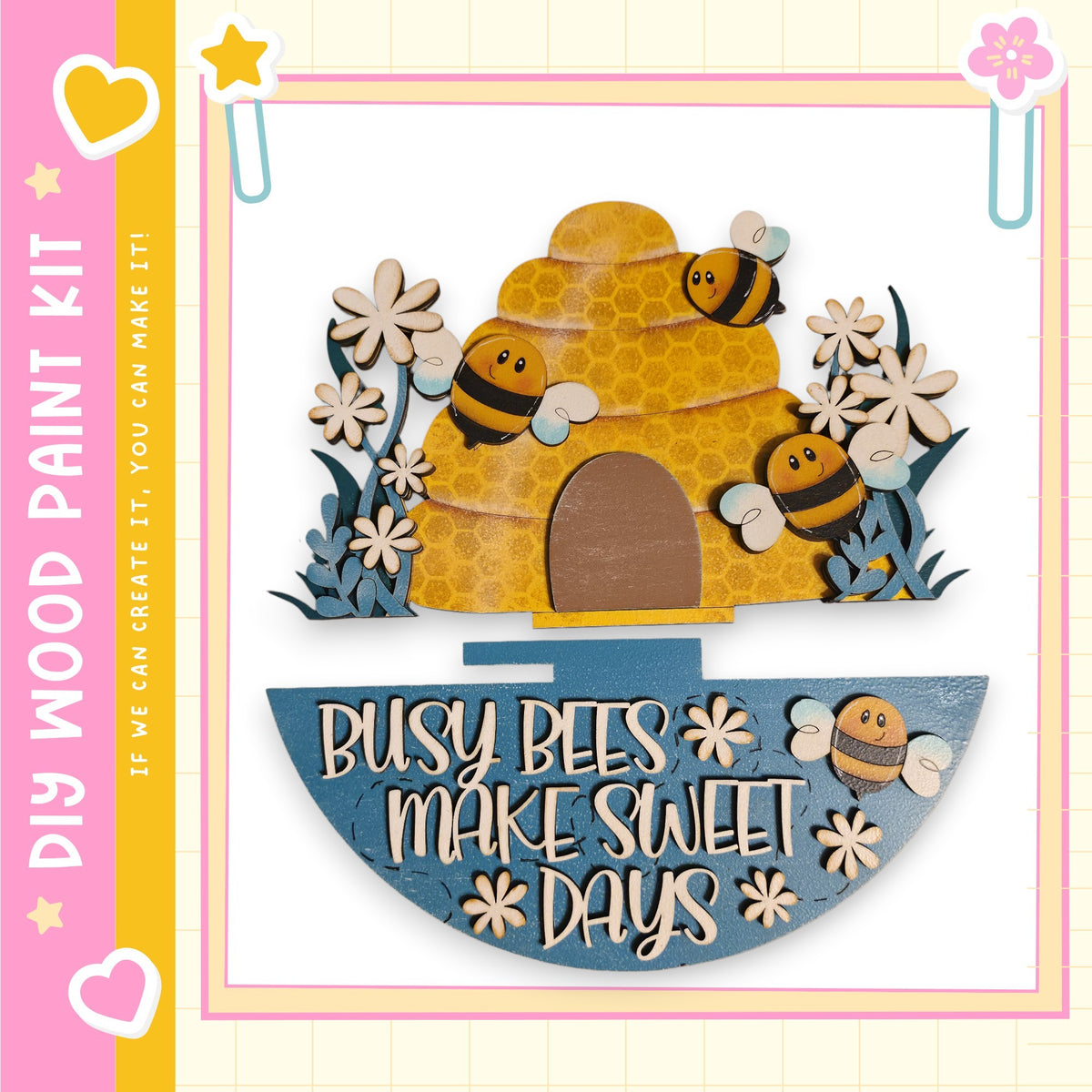 A wooden bee hive with three bees on top, surrounded by flowers and a sign that says "Busy bees make sweet days".