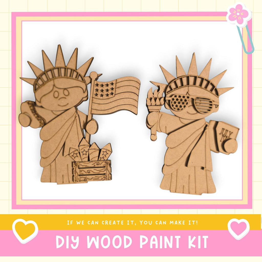 two cardboard cutouts of the Statue of Liberty, one holding an American flag and the other holding a torch, set against a pink and white background.