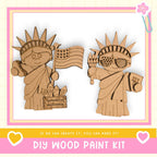 two cardboard cutouts of the Statue of Liberty, one holding an American flag and the other holding a torch, set against a pink and white background.