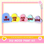 a DIY wood paint kit with a heart-shaped design and the text "BE MINE KISS ME HUG ME XOXO LOVE" written on it.