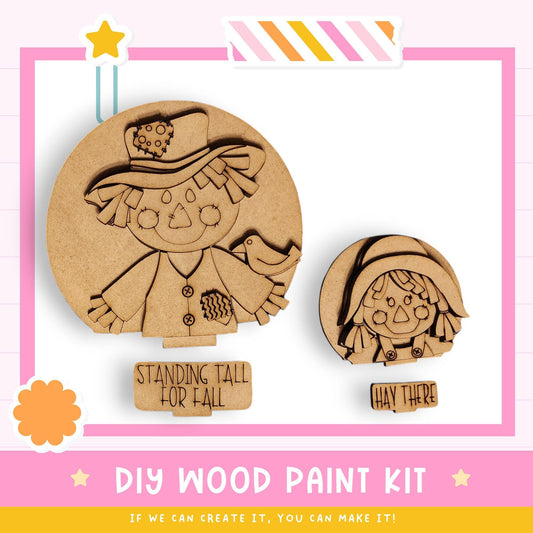 a DIY wood paint kit, including two wooden cutouts of scarecrow figures and a label that says "STANDING TALL FOR FALL".