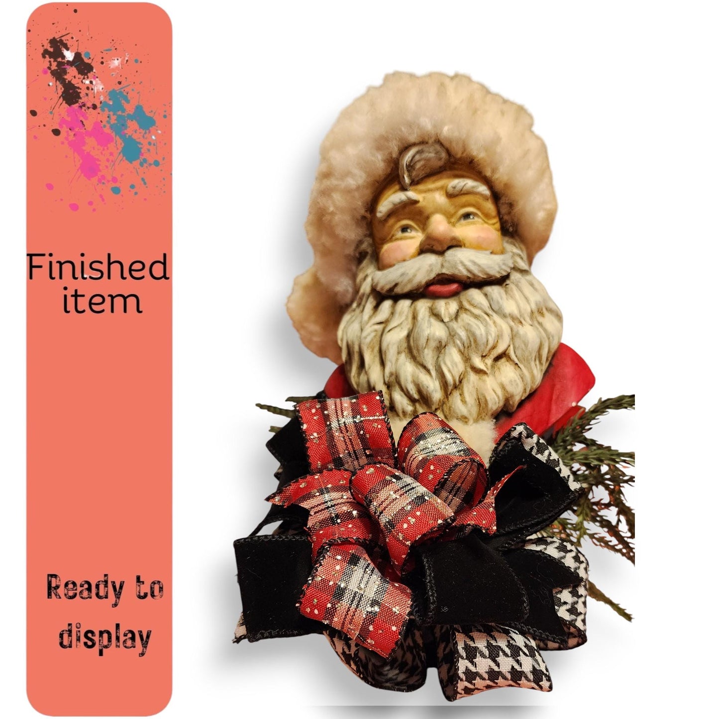 a Santa Claus figurine with a large, fluffy white hat and a red and black plaid bow. The Santa Claus is holding a red and black plaid bow and is surrounded by greenery. The image is described as "finished item" and "ready to display", indicating that it is a completed ornament or decoration.