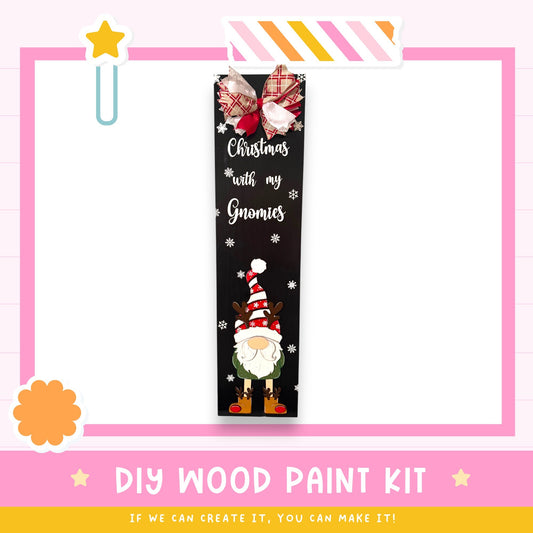 The image is a promotional poster for a DIY wood paint kit, featuring a black banner with a Christmas-themed design and a gnome illustration.