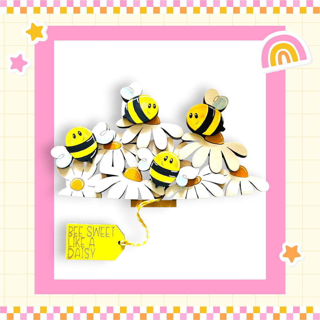 A cheerful arrangement of wooden bees on white flowers, with a yellow tag that reads "Bee Sweet Like a Daisy".