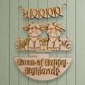 a wooden sign with a banner and two cartoon cow figures, along with the text "Home of Happy Highlands".