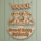 a wooden sign with a banner and two cartoon cow figures, along with the text "Home of Happy Highlands".