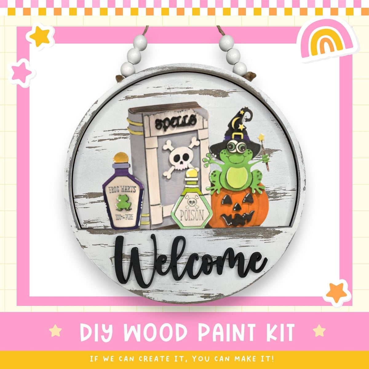 a DIY wood paint kit for creating a welcome sign. The kit includes a wooden sign with a cartoon frog, a skull and crossbones, a bottle of frog juice, and a pumpkin. The kit also includes the text "Welcome" and "DIY WOOD PAINT KIT" along with a rainbow and stars.