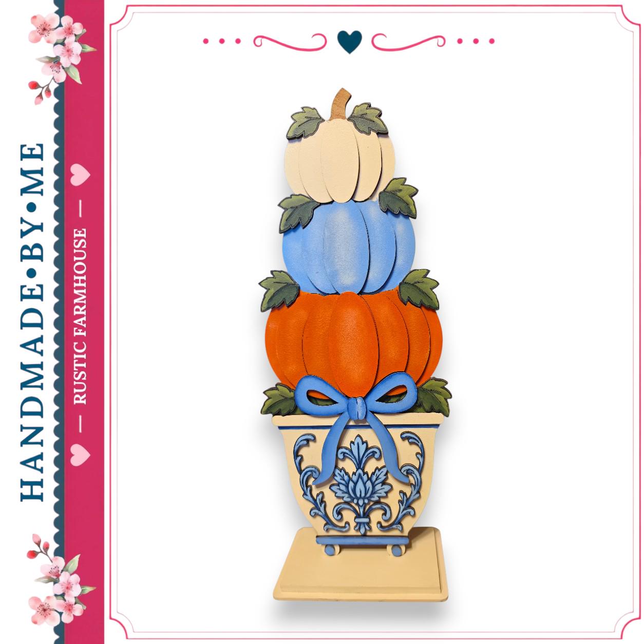 A hand-made wooden pumpkin display with three stacked pumpkins in a decorative vase, featuring a blue bow around the vase.