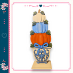 A decorative arrangement of three stacked pumpkins in a vase, with a blue bow tied around the vase.