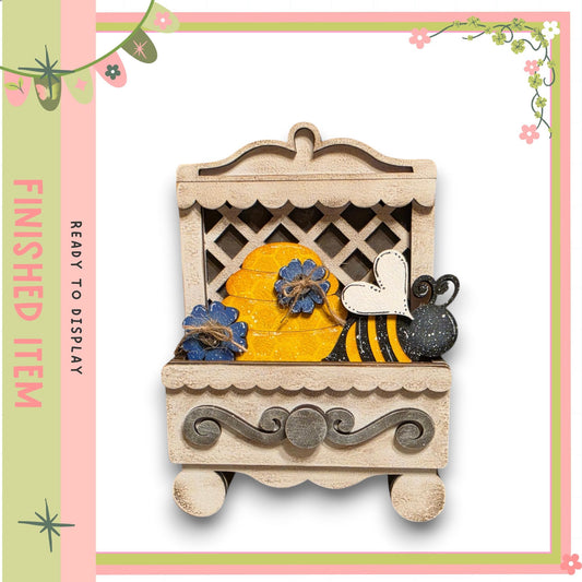 A wooden box with a decorative design, featuring a bee and flowers inside.