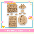 various wooden shapes and decorations, including a bat-shaped object, a sign that says "I'm Batty for Halloween", and a sign that says "Just Hang In Around for Tricks & Treats". The image also includes a DIY wood paint kit and a rainbow-colored object.