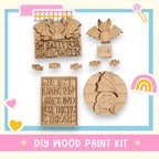 various wooden shapes and decorations, including a bat-shaped object, a sign that says "I'm Batty for Halloween", and a sign that says "Just Hang In Around for Tricks & Treats". The image also includes a DIY wood paint kit and a rainbow-colored object.