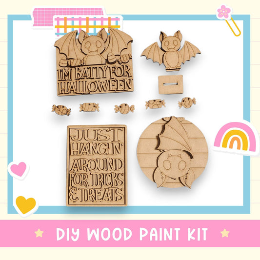 various wooden shapes and decorations, including a bat-shaped object, a sign that says "I'm Batty for Halloween", and a sign that says "Just Hang In Around for Tricks & Treats". The image also includes a DIY wood paint kit and a rainbow-colored object.