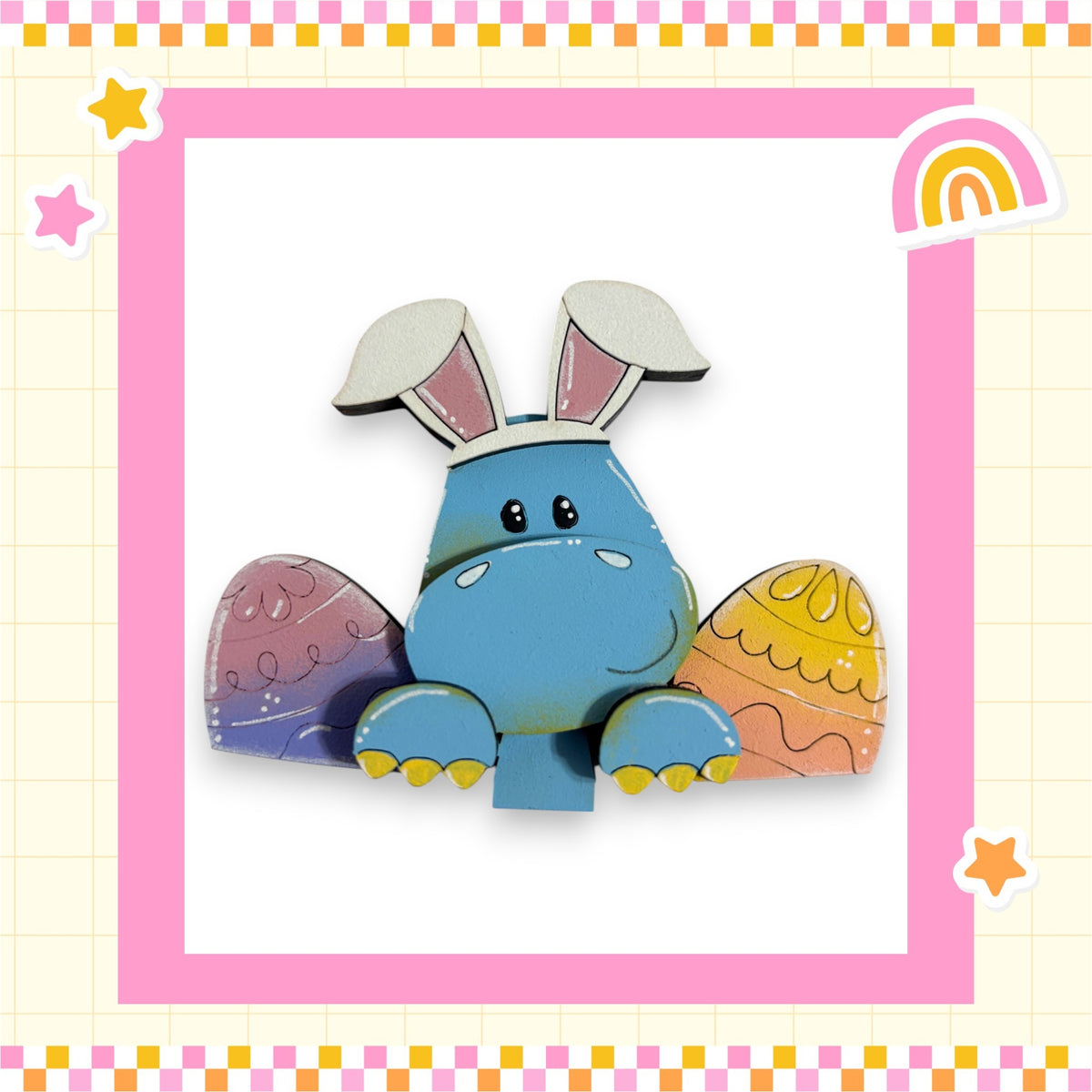 A blue cartoon rabbit with large ears and a smiling face is sitting in the center of a pink and yellow checkered border, surrounded by Easter eggs and stars.