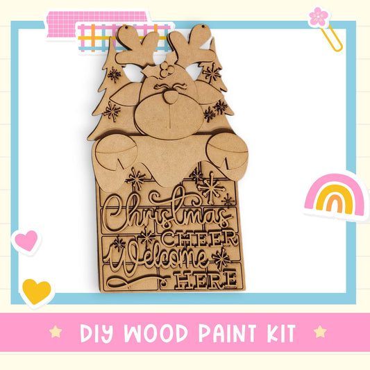 A DIY wood paint kit for creating a Christmas-themed sign, featuring a wooden reindeer and the text "Christmas cheer welcome here".