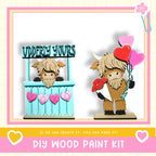 two wooden toy animals, one holding heart-shaped balloons, and the other sitting in a booth with a sign that says "VUDDERY YOURS". The image also includes text that says "DIY WOOD PAINT KIT" and "IF WE CAN CREATE IT, YOU CAN MAKE IT!"